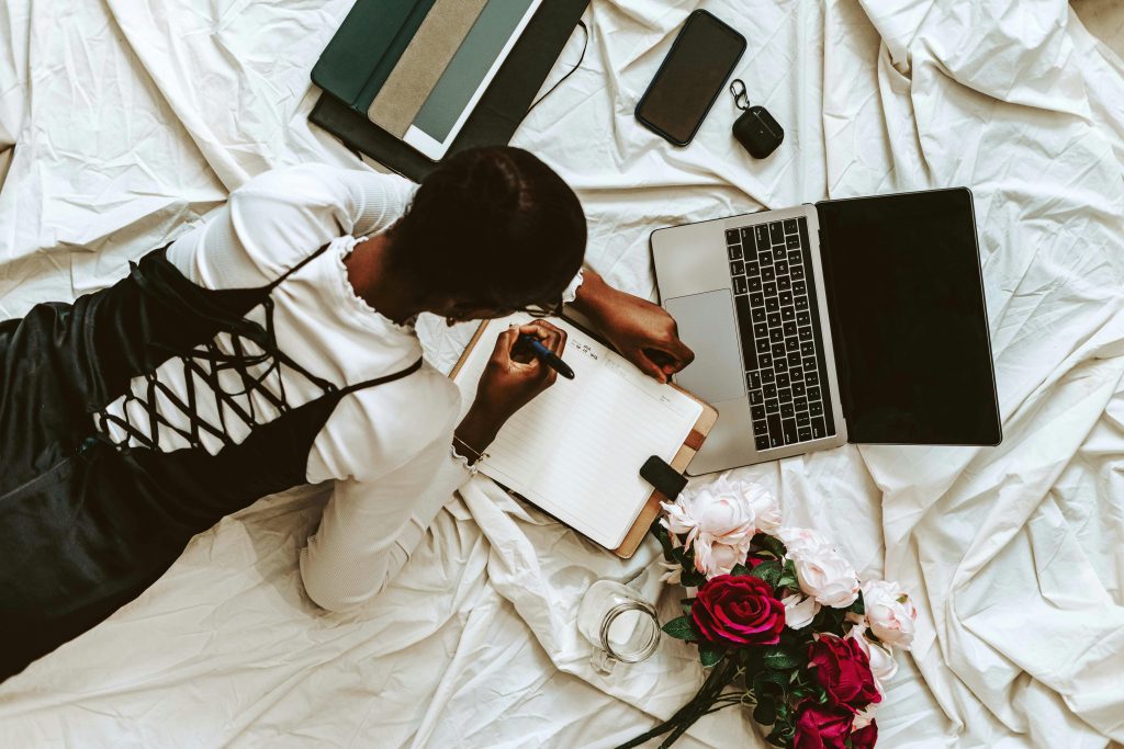 African woman working remotely on laptop with notebooks and flowers around. Comfortable home setup.