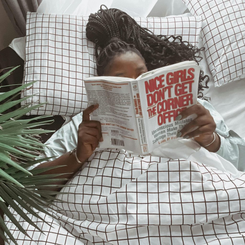 A woman enjoys a quiet moment reading in bed, covered with a stylish grid-patterned blanket.